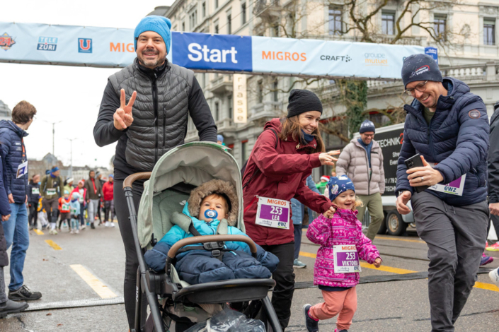 A group of people taking part in a race with a baby in a baby carriage.