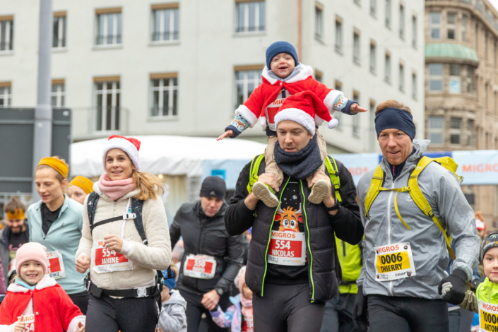 A group of people wearing Christmas hats run through a city.