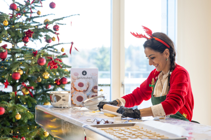 A woman bakes cookies in front of a Christmas tree.
