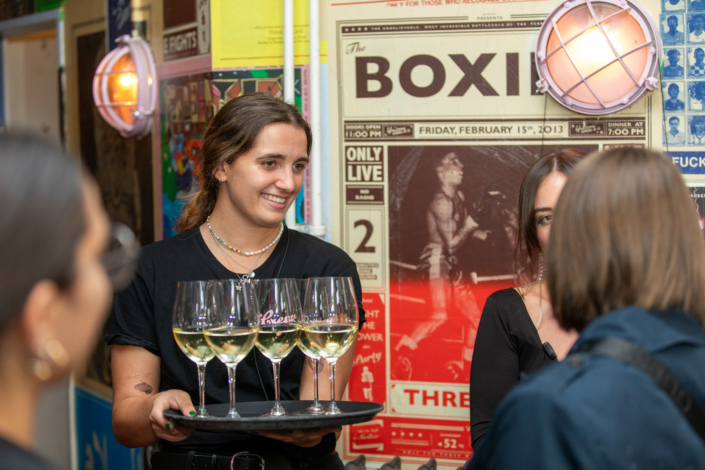 A group of women hold wine glasses in front of a poster.
