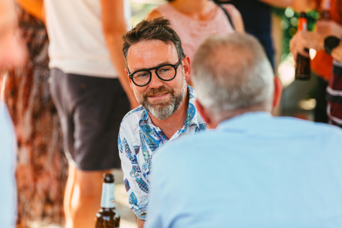 Ein Mann mit Brille spricht bei einer Veranstaltung im Freien mit einer Gruppe von Menschen.