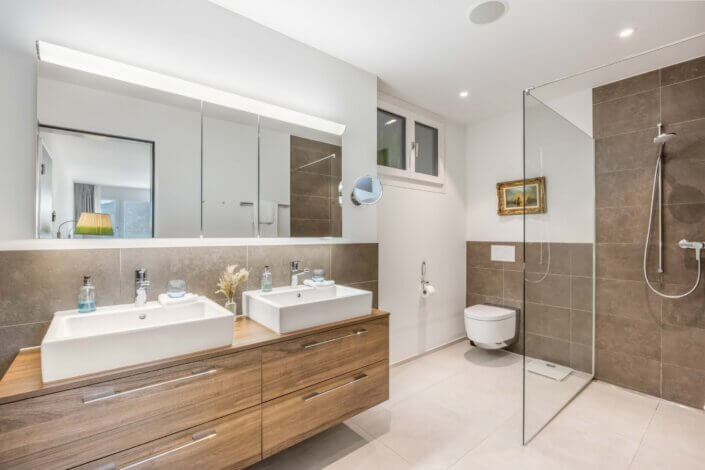 Modern bathroom with double washbasin, large mirrors, wall-mounted WC and walk-in shower with glass screen. Brown and white color scheme, small mural and window available.