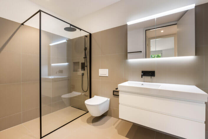 Modern bathroom with glazed shower, wall-mounted WC, floating washbasin with washbasin, mirror cabinet and ceiling lighting. Walls and floor in neutral tiles.