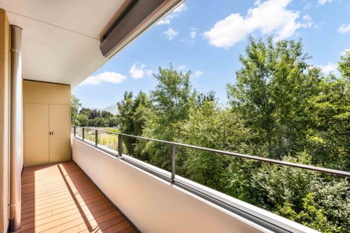 A wooden-floored balcony overlooks a lush green forest under a partly cloudy sky.